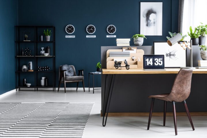 Contemporary home office with dark blue walls, wooden desk, laptop clock showing 14:35, and plants.